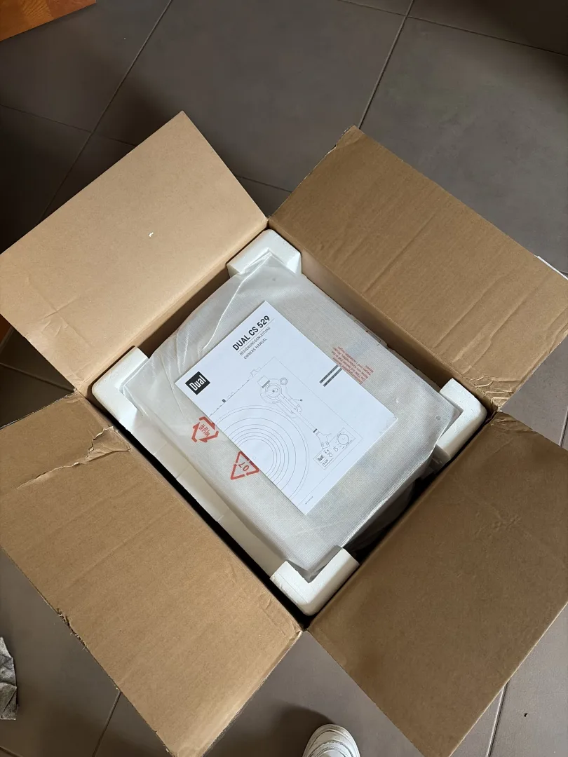Carton ouvert contenant la platine vinyle Dual CS 529 BT calée dans sa protection en polystyrène avec la notice par-dessus