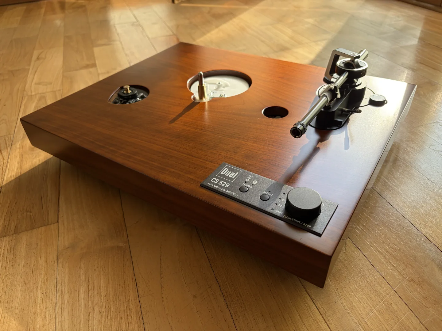 Platine vinyle Dual CS 529 BT sans plateau, vue en angle sur un parquet avec le bras de lecture et le panneau de commande