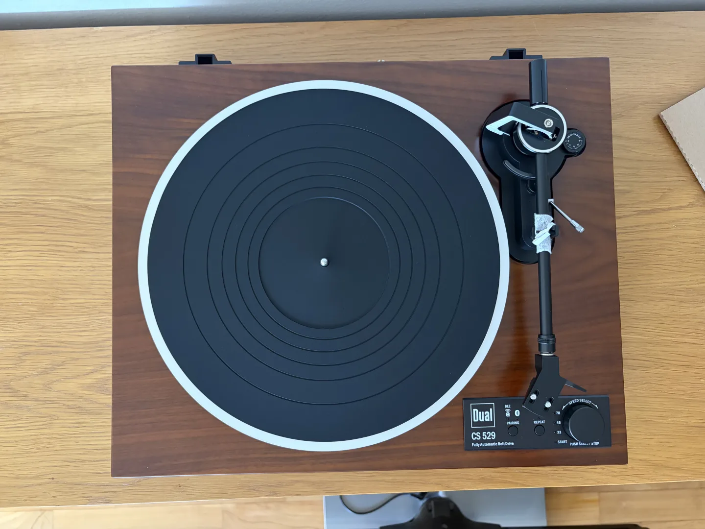 Vue du dessus de la platine Dual CS 529 BT avec son plateau, son tapis en caoutchouc et son bras de lecture, posée sur un meuble en bois