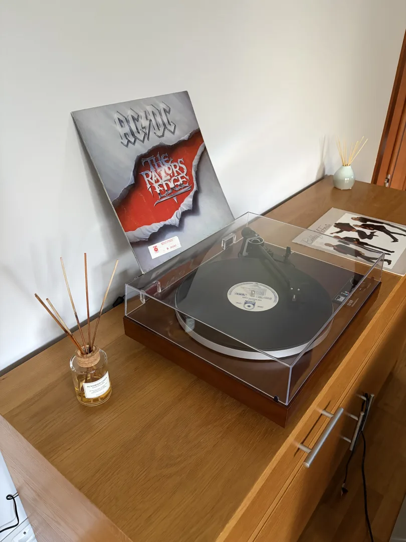 Platine Dual CS 529 BT avec son capot posée sur un meuble en bois, à côté de pochettes de vinyles et d'un diffuseur de parfum d'ambiance