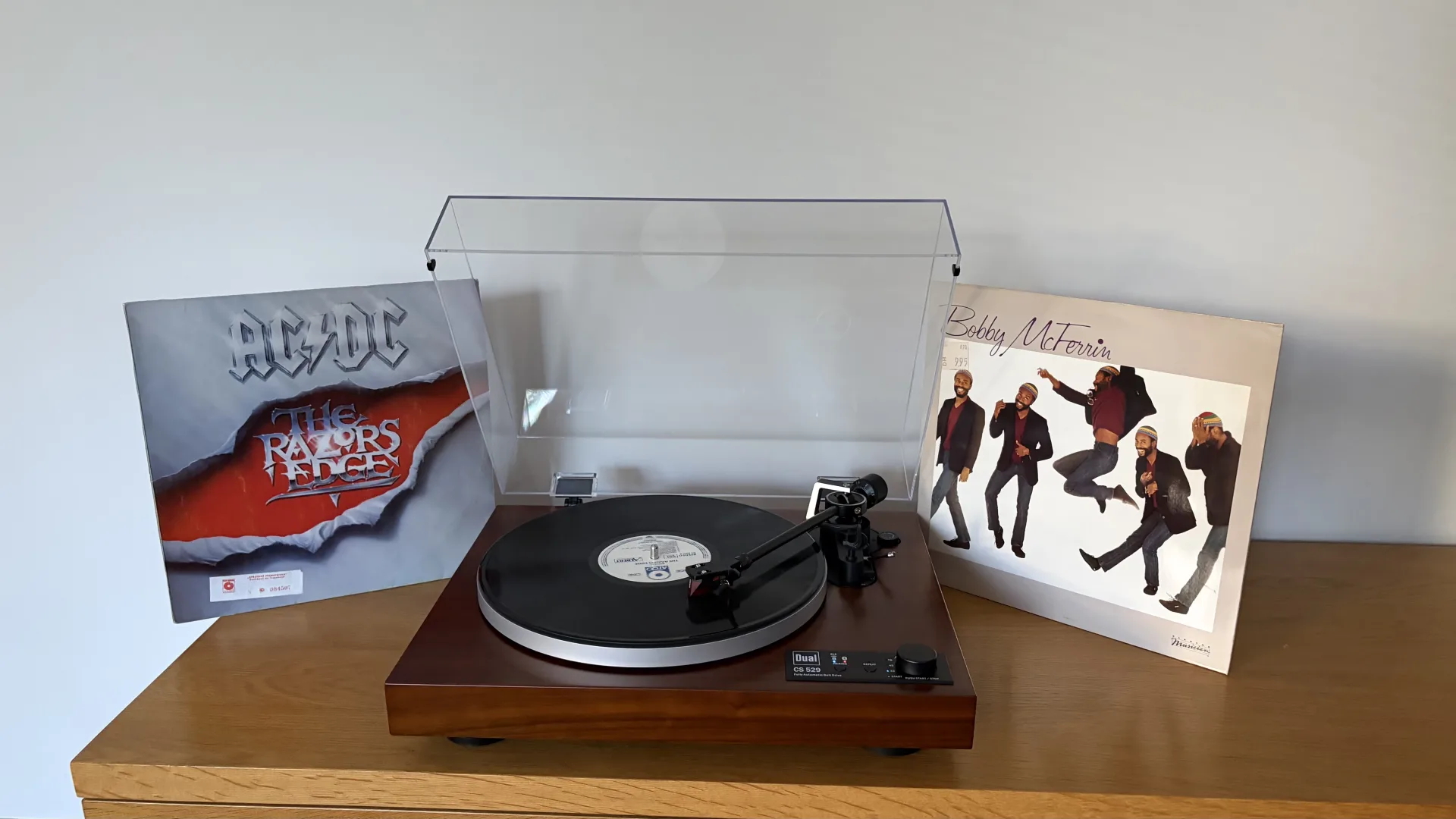 Platine vinyle Dual CS 529 BT à finition bois posée sur un meuble, avec son capot transparent et deux pochettes de vinyles à ses côtés