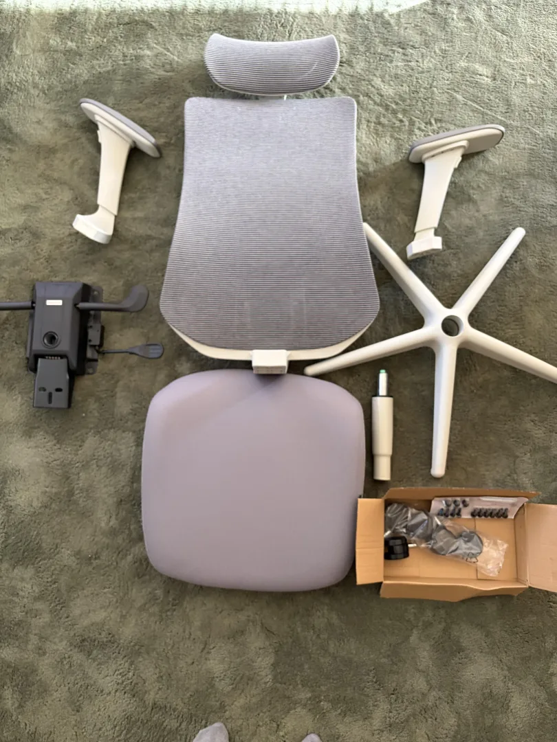 Pièces de la Desktronic SitOne déballées avant montage : base, vérin, mécanisme, assise, dossier, accoudoirs et appui-tête