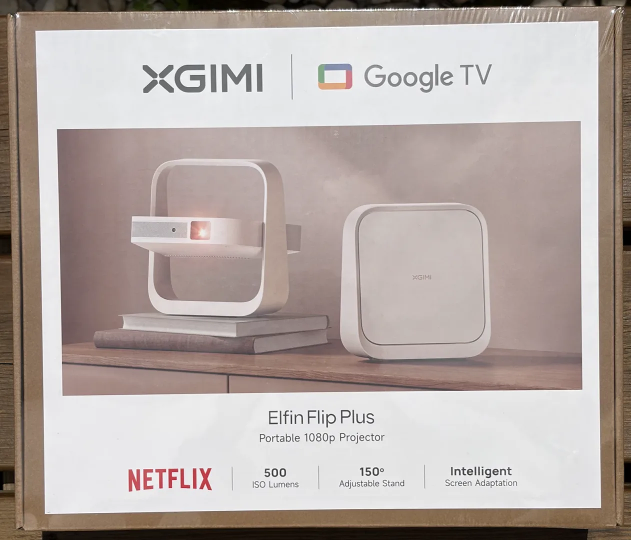 Boîte du vidéoprojecteur portable XGIMI Elfin Flip Plus sur une terrasse en bois