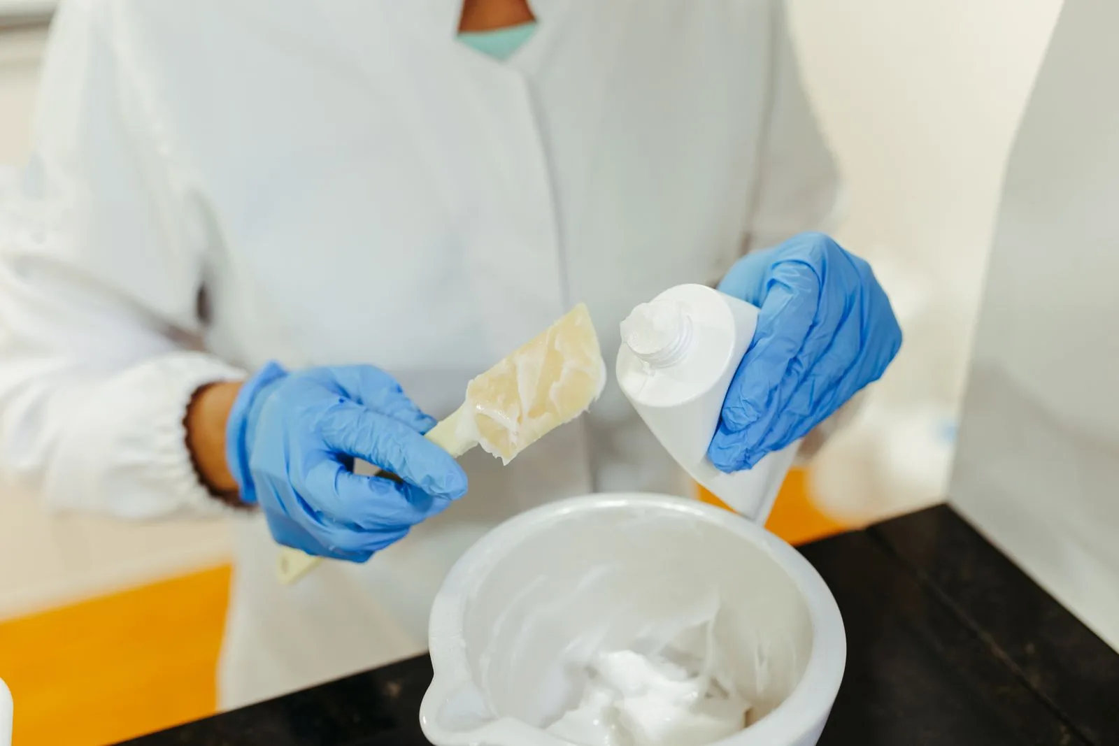 Technicien en gants mélangeant une crème dans un bol dans un laboratoire de tests cosmétiques